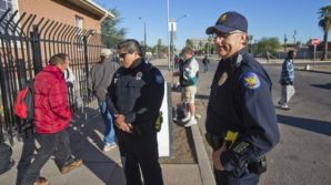 Phoenix police officers Esteban Navarrette (left) and Lee Williams monitor homeless individuals  at 12th Avenue and Madison Street in downtown Phoenix. Central Arizona Shelter Services has opened a parking lot there where the homeless can sleep called the "overflow". The city of Phoenix Police Department has expanded patrols in the area to mange the problem.  Picture credit: Tom Tingle